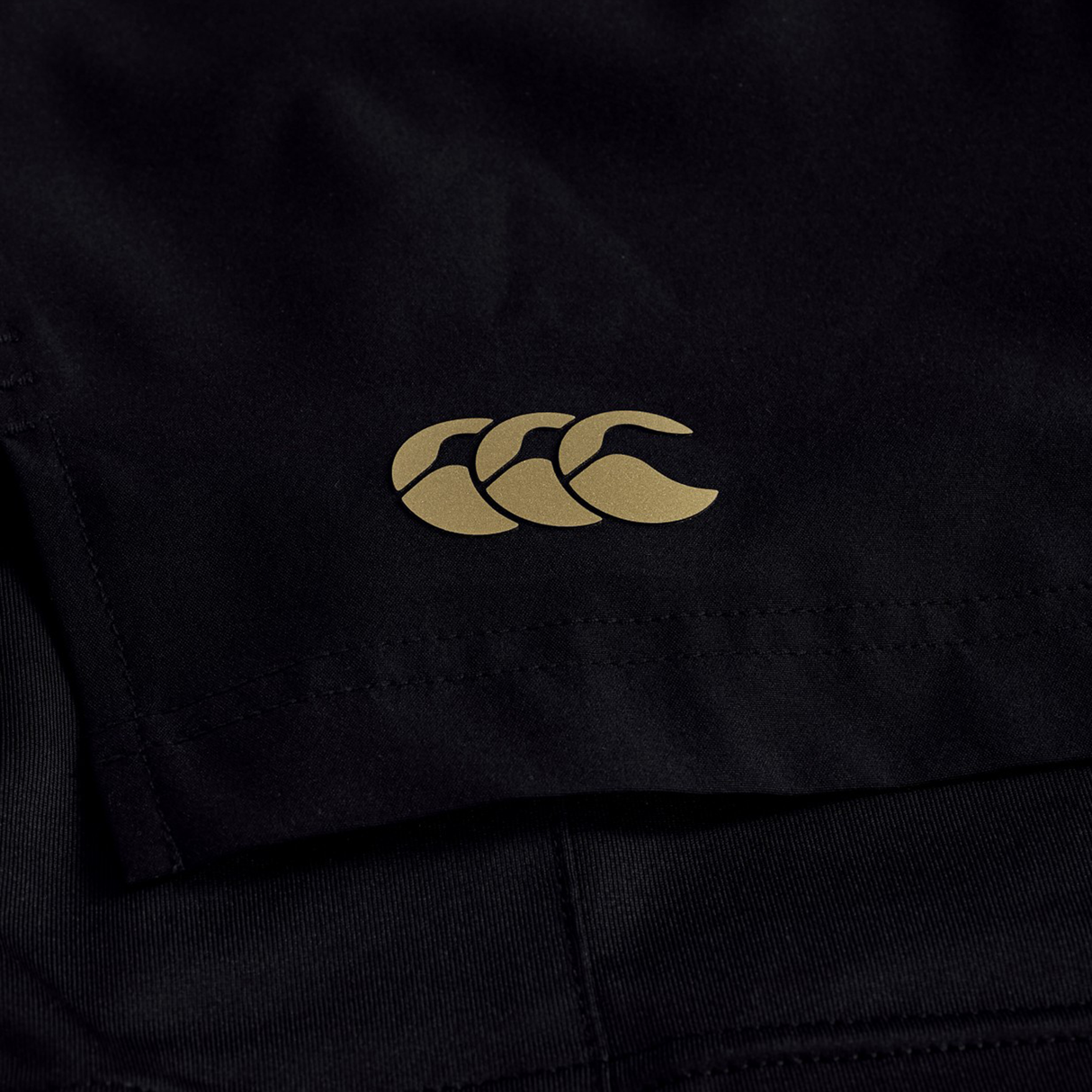 Close-up of black Canterbury Tempo+ 5" 2-In-1 Shorts, featuring a gold Canterbury logo with three overlapping stylized Cs.