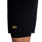 Close-up of a person's lower thigh wearing Canterbury Tempo+ 5" 2-In-1 Shorts, showing a small yellow logo on the side and a visible inner black layer.