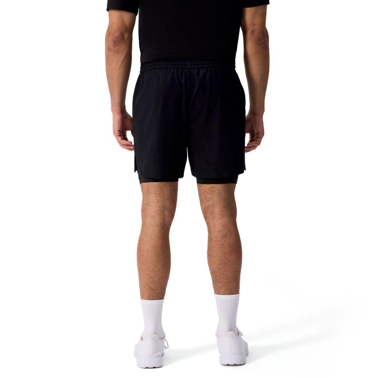A man stands facing away against a plain white background, wearing a black t-shirt, Canterbury Tempo+ 5" 2-In-1 Shorts, white socks, and white shoes.