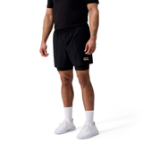 A man stands against a white background wearing a black t-shirt, Canterbury Tempo+ 5" 2-In-1 Shorts with logo, white socks, and white sneakers.