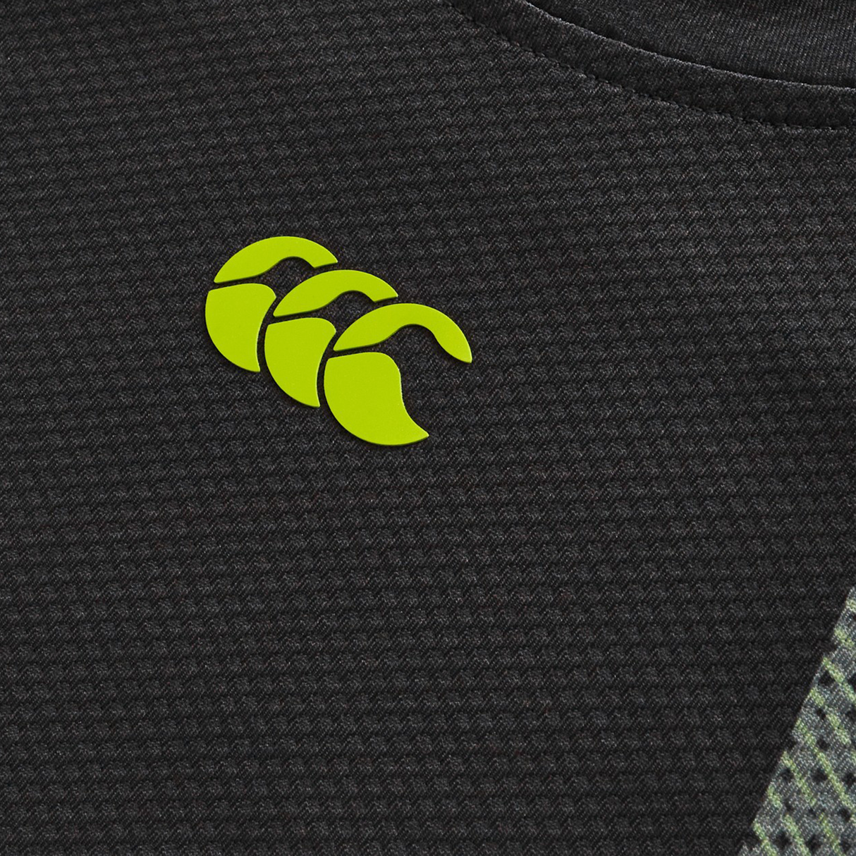 Close-up of the textured black Canterbury H225 fabric featuring a yellow logo with three overlapping "C"s, as seen on the Canterbury Tempo+ Training Tee.