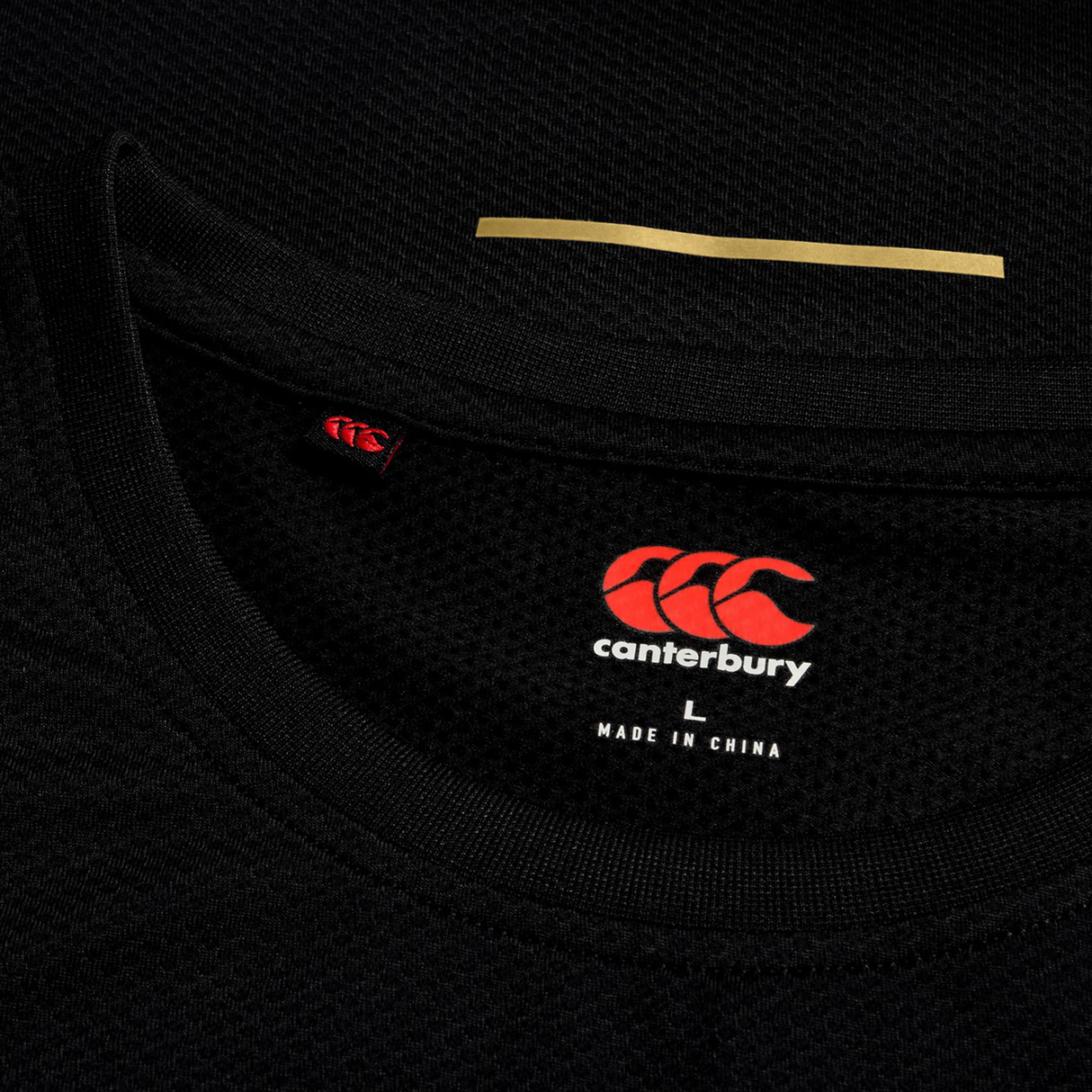 Close-up of the collar and tag on a black Canterbury Tempo+ Training Tank, highlighting its athletic fit, red and white Canterbury logo, size L, and "Made in China" text.
