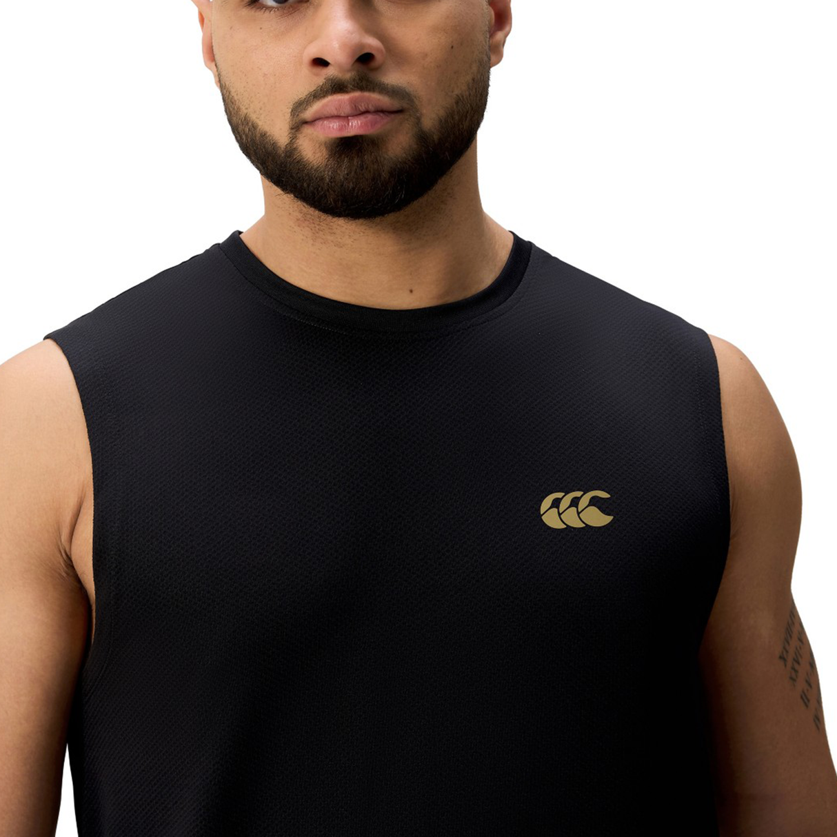 A man stands against a white background wearing the Canterbury Tempo+ Training Tank, a sleeveless black top featuring a gold logo on the left chest.