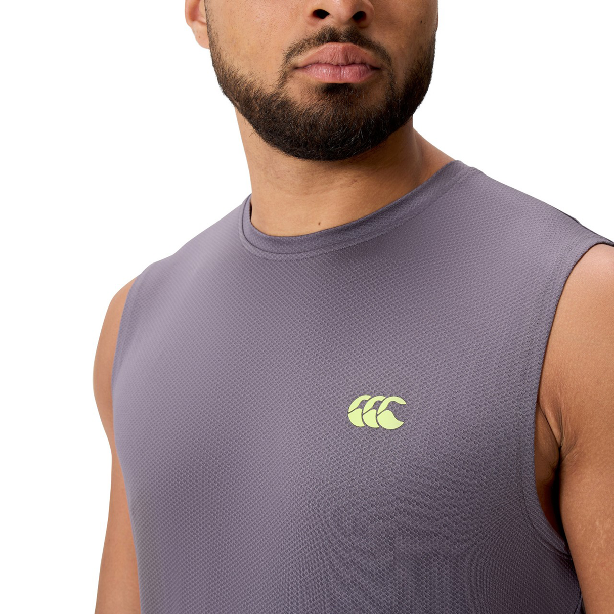 A man wears the Canterbury Tempo+ Training Tank, a sleeveless gray top featuring a small yellow chest logo and moisture-wicking fabric for optimal comfort.