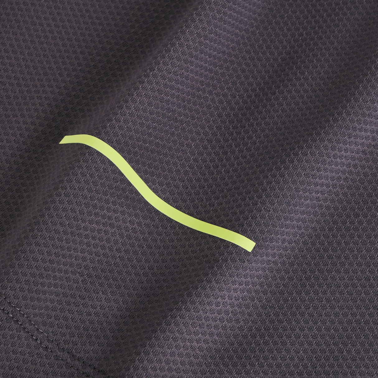 Close-up of textured dark gray fabric from the Canterbury Tempo+ Training Tank, featuring a single yellow wavy line and moisture-wicking properties.