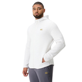 A man wearing the Canterbury Everest Training Full-Zip Hoodie in white with a gold logo and gray athletic pants stands with one hand in his pocket against a plain white background.