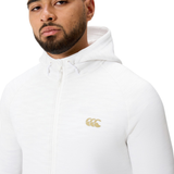 A man wears the white Everest Training Full-Zip Hoodie by Canterbury, featuring a gold Canterbury logo on the chest, as he looks slightly to the side.