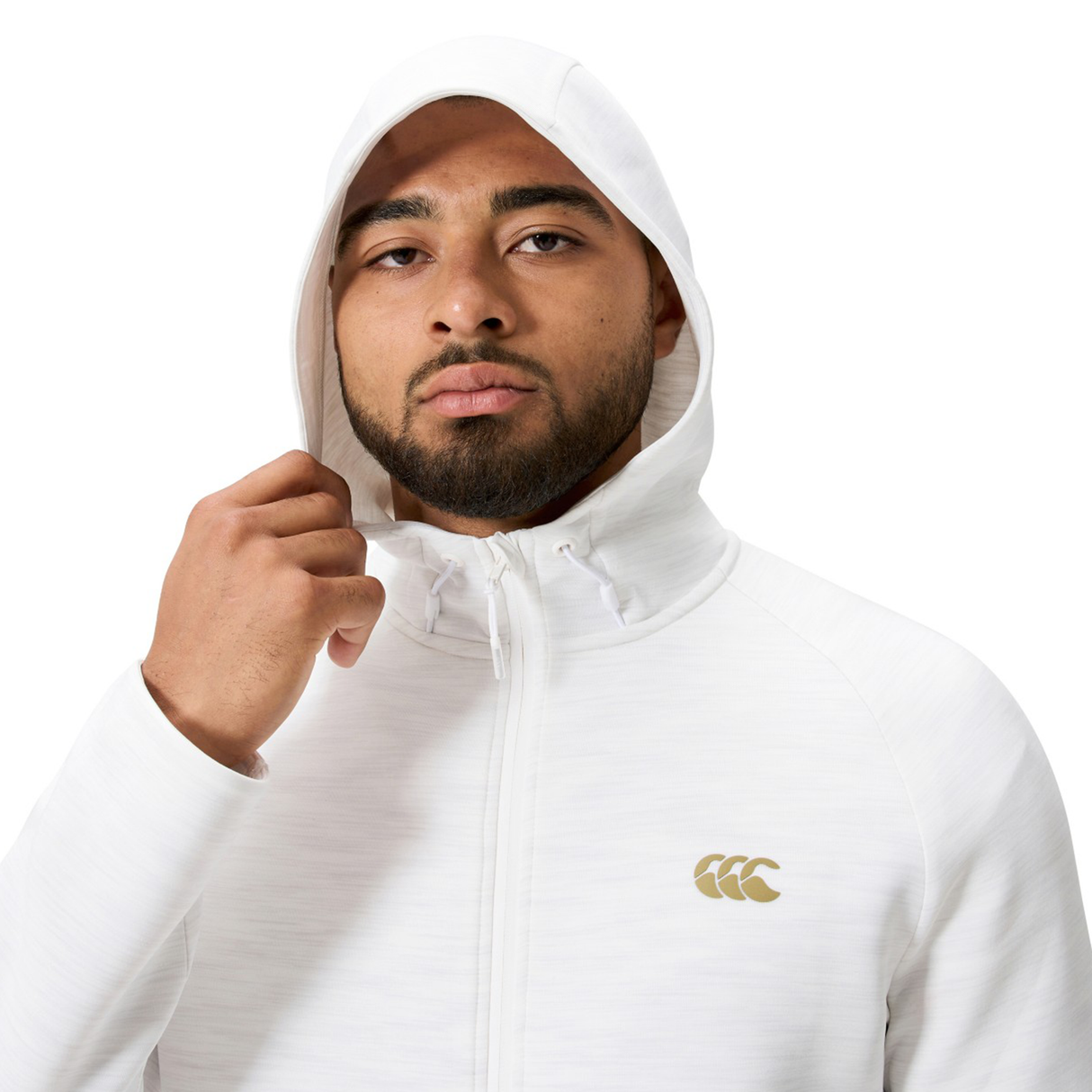 A man with a trimmed beard wears the Everest Training Full-Zip Hoodie by Canterbury in white, holding the hood with one hand. The hoodie features a small gold Canterbury logo on the chest.