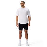 A man stands against a white background wearing the Everest Training Tee by Canterbury, black shorts, white socks, and white sneakers. This Canterbury shirt offers a performance fit ideal for intense training. He is looking to the side.