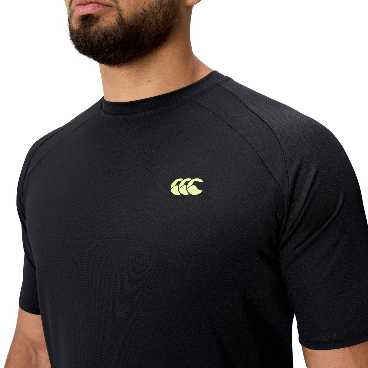 A person wearing the black Everest Training Tee by Canterbury, featuring a yellow Canterbury logo on the chest, designed for rugby players who want a performance fit.