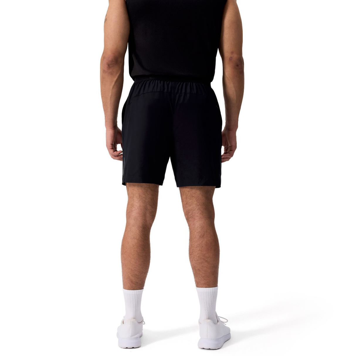 A man faces away, wearing a black sleeveless shirt and Canterbury Tempo+ 7" Training Shorts, paired with white socks and sneakers, against a plain white background.
