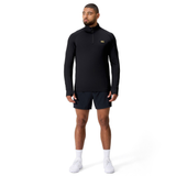 A man faces slightly to the side, wearing a black Canterbury Tempo+ 1/4 Zip Training Top, black shorts, white socks, and white sneakers against a plain white background.