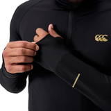 A person adjusts the sleeve of a Canterbury Tempo+ 1/4 Zip Training Top in black, featuring a yellow logo and yellow forearm stripe, with thumb holes and long sleeves.