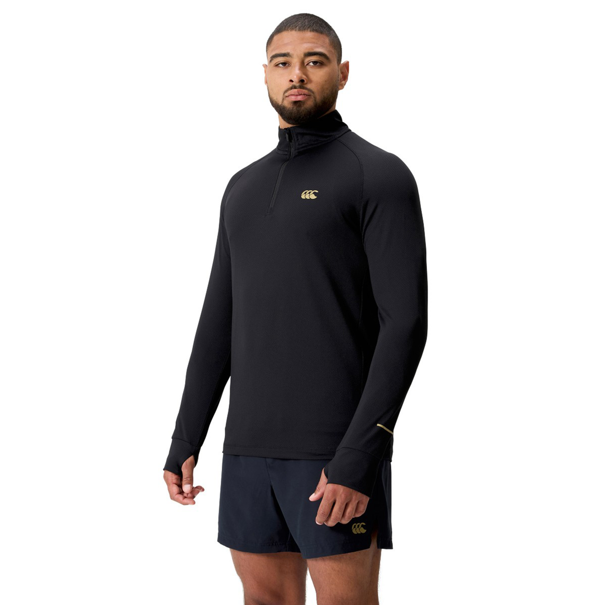 A man in a black Canterbury Tempo+ 1/4 Zip Training Top and black shorts stands against a white background.