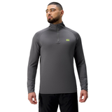 A man faces forward, wearing a gray Canterbury Tempo+ 1/4 Zip Training Top featuring a small green chest logo, paired with black pants.