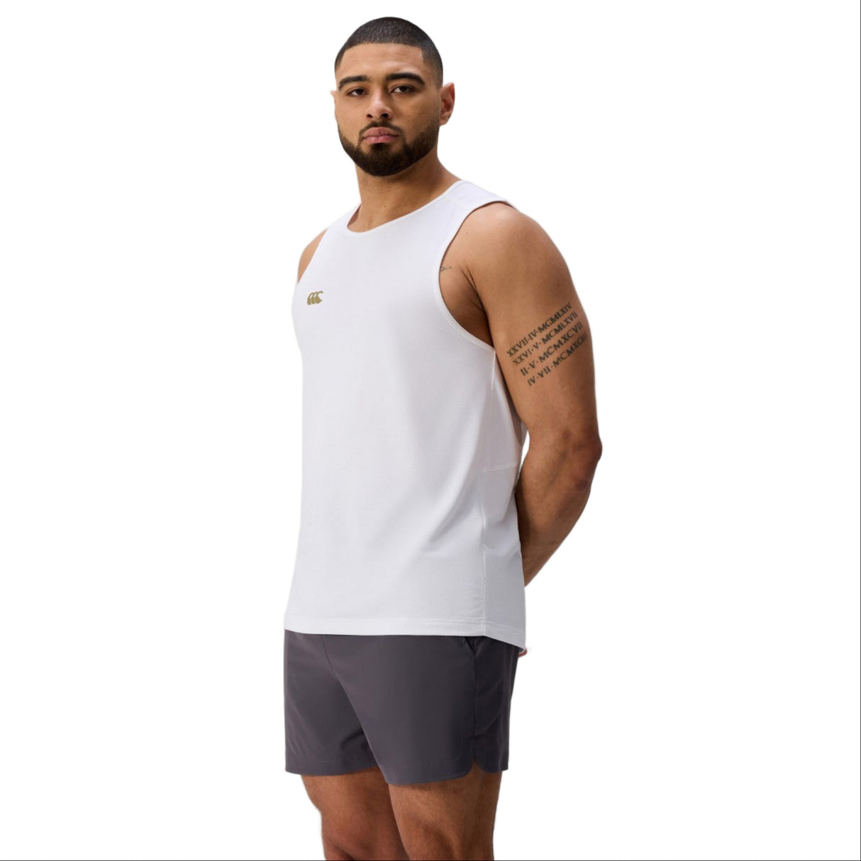 A man with short hair and a beard wears the white Tempo+ Singlet by Canterbury and dark athletic shorts, standing against a plain light background.