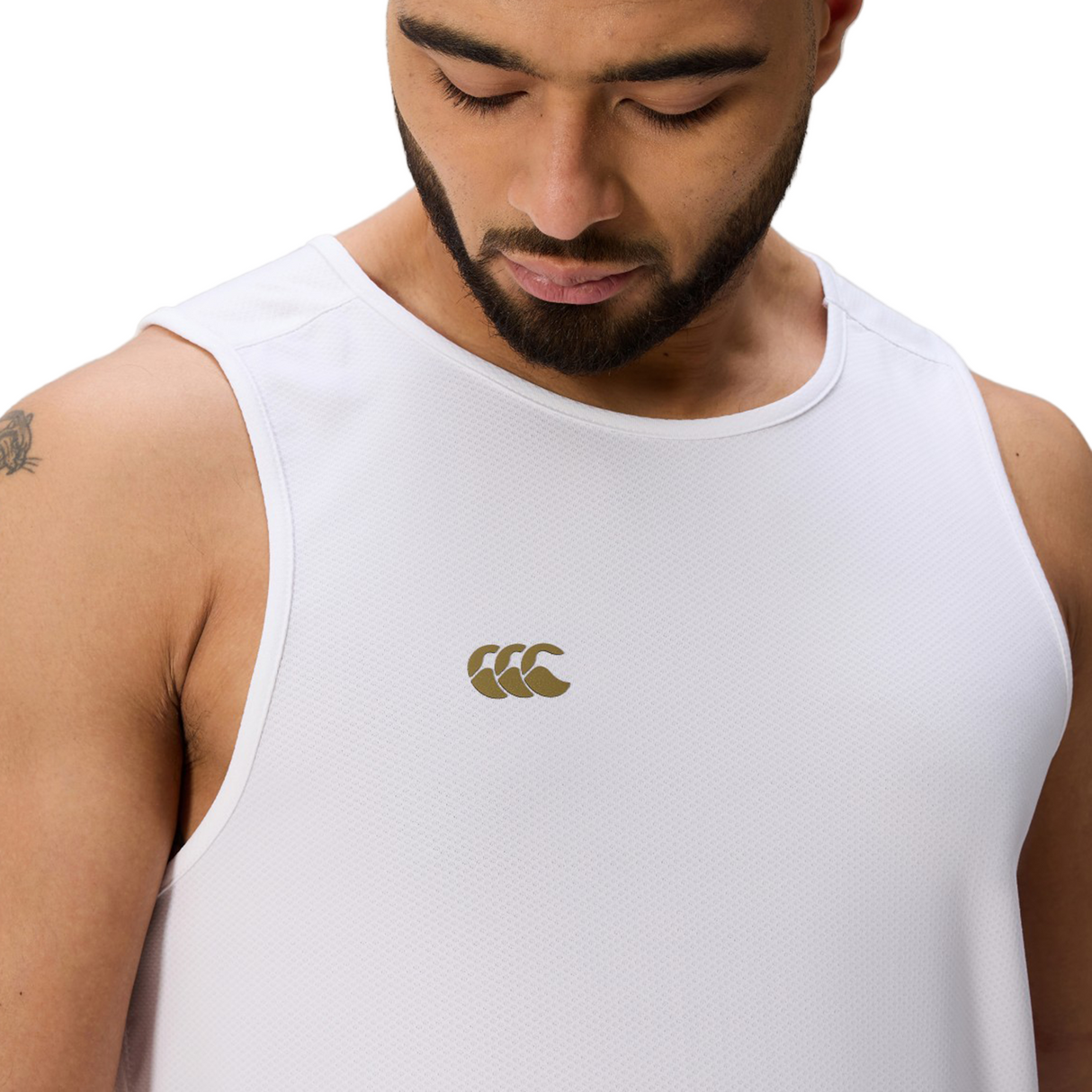 A man wearing the white Tempo+ Singlet by Canterbury with a gold brand logo looks down.