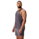 A man stands in an athletic pose wearing the gray Tempo+ Singlet by Canterbury and matching shorts, looking left with a tattoo visible on his upper right arm.