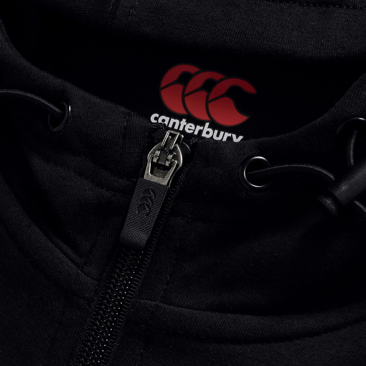Close-up of the Canterbury Tempo+ Full-Zip Hoodie in black, featuring drawstrings, a red Canterbury logo, and "canterbury" text on the inside collar—a lightweight stretch hoodie ideal for rugby warm-ups.