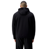 Someone wearing the Canterbury Tempo+ Full-Zip Hoodie in black stands with their back to the camera, paired with black pants against a white background.
