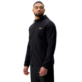 A man wearing a black Canterbury Tempo+ Full-Zip Hoodie and black pants stands facing slightly to the side against a white background.