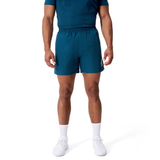 A man wearing a blue t-shirt, Canterbury Uglies Logo Tactic Shorts, white socks, and white sneakers stands against a plain white background.
