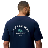 A man wears the Canterbury Sport Dept. Logo T-Shirt, an athletic cotton blend tee by Canterbury with "Sport Dept 1904" and logo printed on the back.