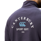 Close-up of a person wearing the Sport Dept. 1/4 Zip Sweater by Canterbury, featuring "Sport Dept 1904" and a blue logo on the back.