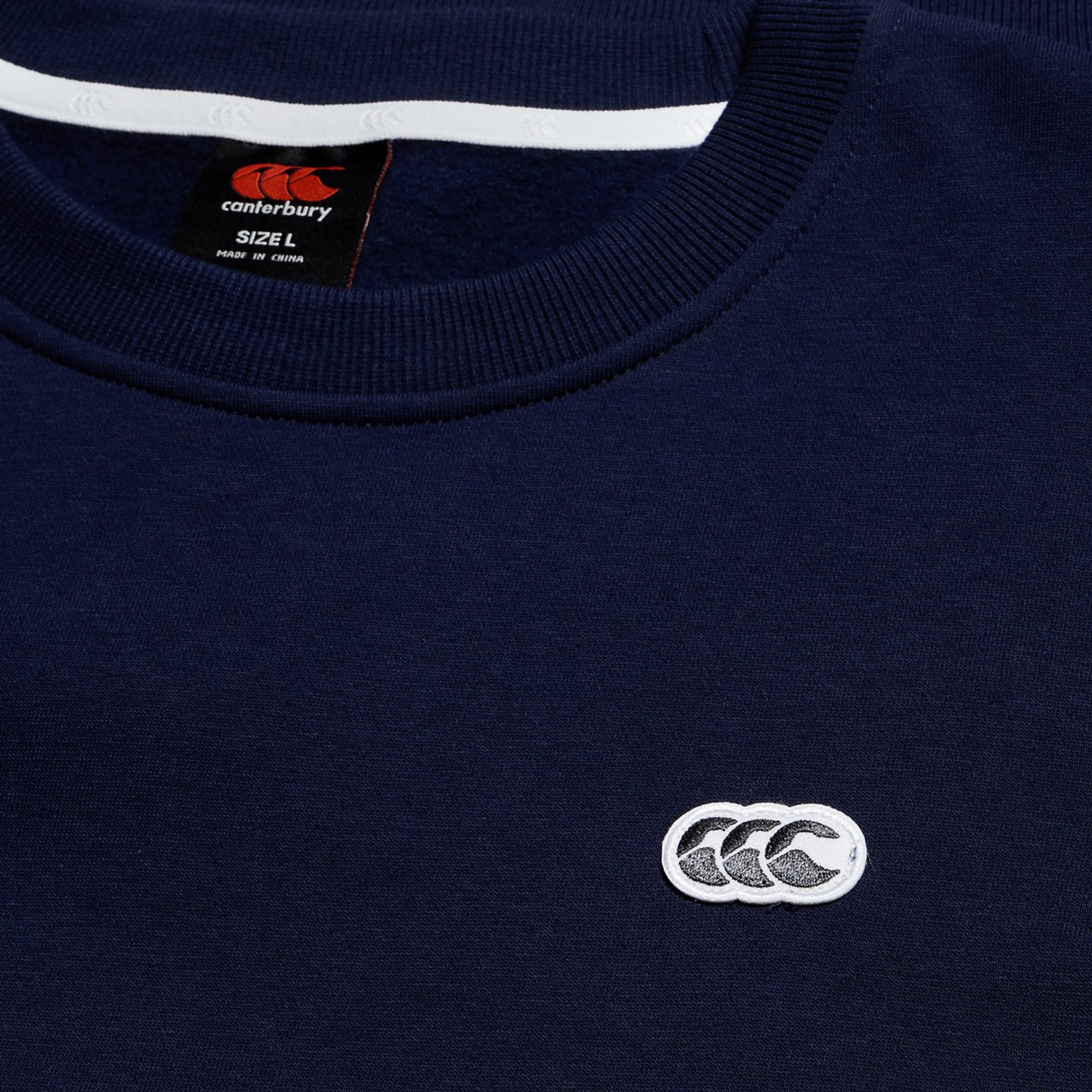 Close-up of the Sport Dept. Crew Sweatshirt by Canterbury in navy blue, featuring the white Canterbury logo on the chest and a size label inside the collar.