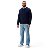 A man faces forward against a plain white background, wearing the navy blue Sport Dept. Crew Sweatshirt by Canterbury, light blue jeans, and white shoes.