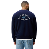 A man faces away, wearing the Canterbury Sport Dept. Crew Sweatshirt featuring "Canterbury Sport Dept 1904" and logo on the back, styled with light blue jeans for an athletic look.