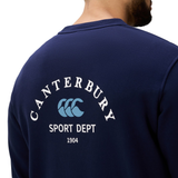 A person wearing the Canterbury Sport Dept. Crew Sweatshirt, a navy blue sweatshirt with "Canterbury Sport Dept 1904" and a blue logo on the back.