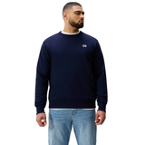 Man in an athletic fit navy Sport Dept. Crew Sweatshirt by Canterbury and light blue jeans, standing with arms relaxed and gazing to the side.