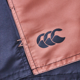 Close-up of Canterbury Women's Fundamentals 3" Harletic Shorts featuring a black Canterbury logo on a brown panel with visible stitching beside a dark blue section—designed for women's rugby and athletic training.