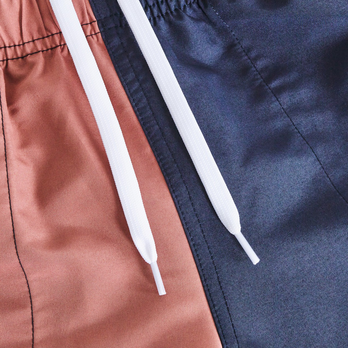 Close-up of the Women's Fundamentals 3" Harletic Shorts by Canterbury, color-blocked with one side brown and the other navy blue, featuring an elastic waistband and white drawstrings.