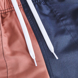 Close-up of the Women's Fundamentals 3" Harletic Shorts by Canterbury, color-blocked with one side brown and the other navy blue, featuring an elastic waistband and white drawstrings.