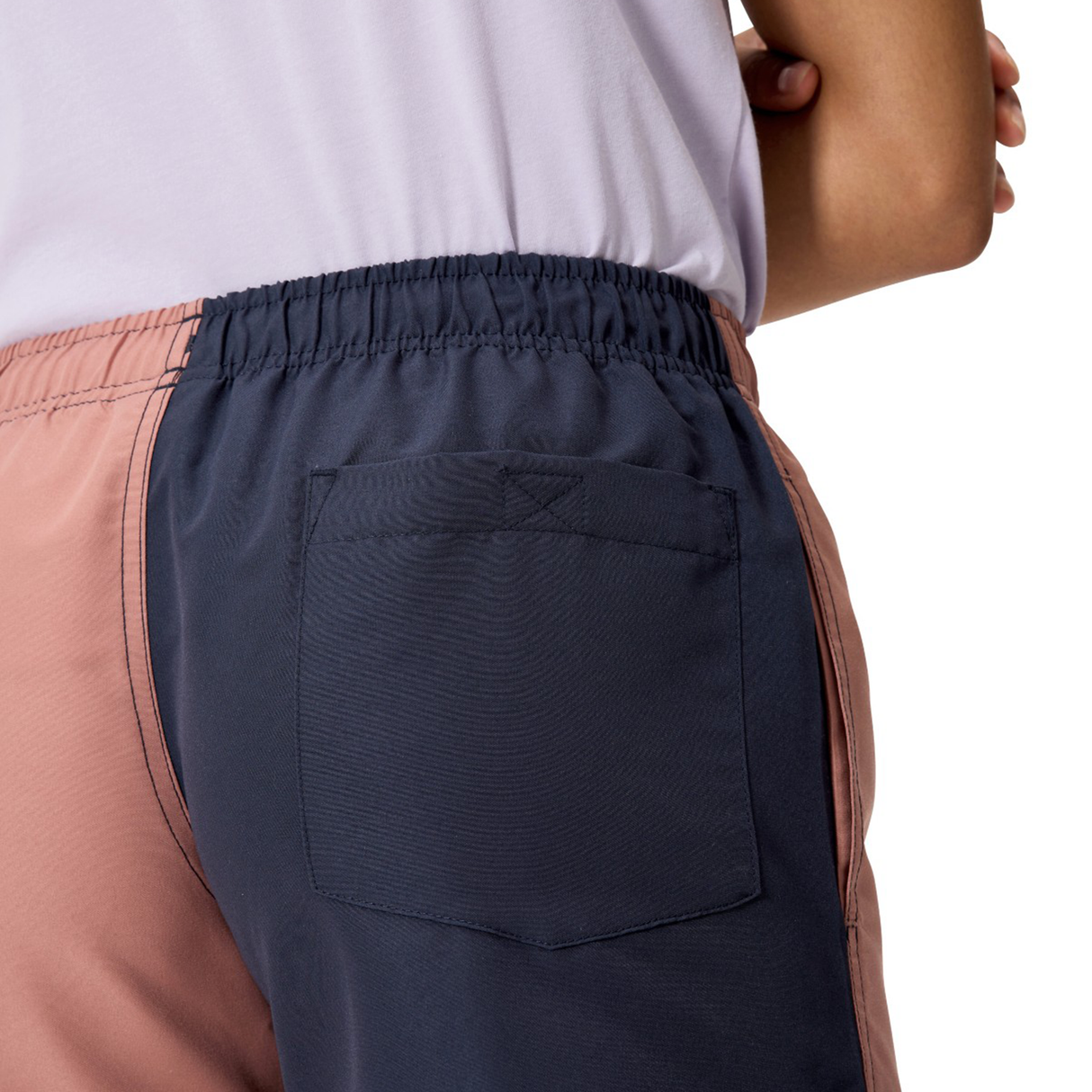 A woman wears Canterbury’s Fundamentals 3" Harletic Shorts, featuring color-blocking, an elastic waistband, and a back pocket, shown from the rear waist down.