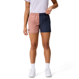 A person in a white t-shirt and Canterbury Women’s Fundamentals 3" Harletic Shorts—half pink, half navy blue—paired with white socks and sneakers, stands against a plain background.