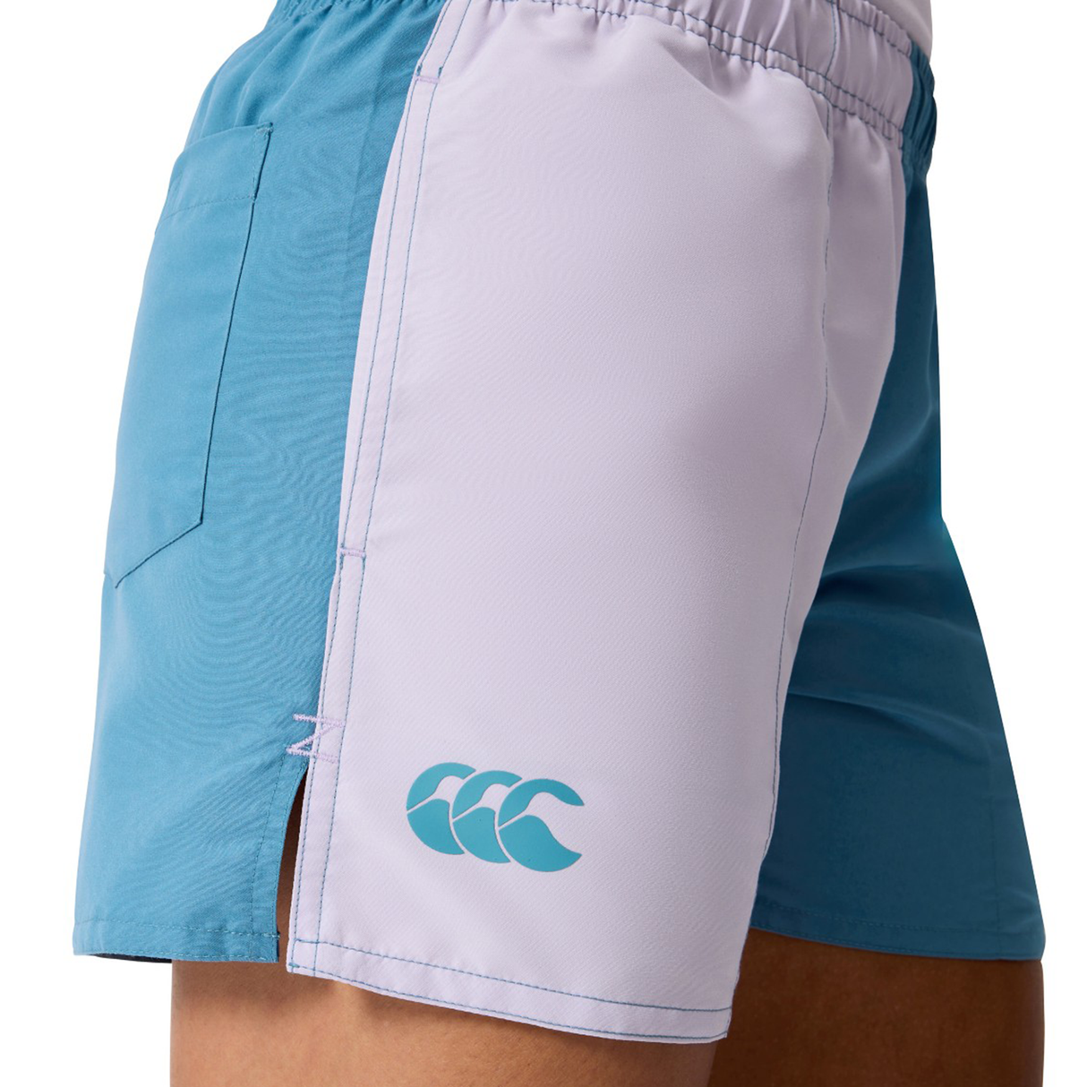 A person wearing Canterbury Women's Fundamentals 3" Harletic Shorts in turquoise and white, featuring an elastic waistband, side pocket, and front CCC logo—ideal for rugby or athletic training.