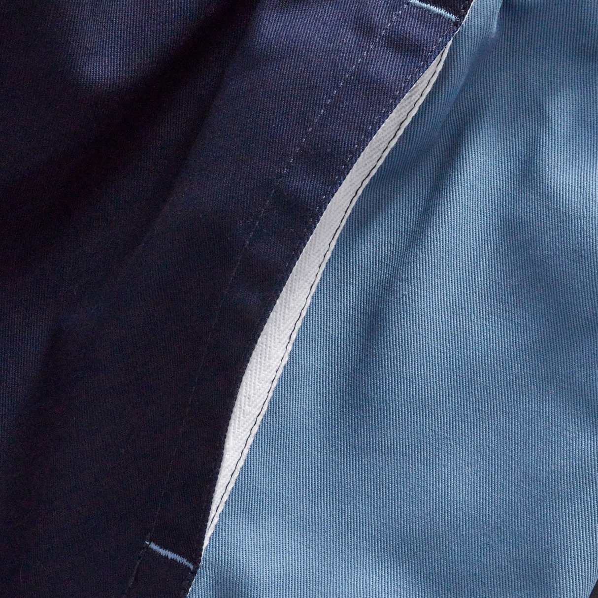 Close-up of a seam on Canterbury's Fundamental Harlequin Drill 3" Shorts, showing navy blue and light blue cotton panels stitched together with a visible white inner lining.