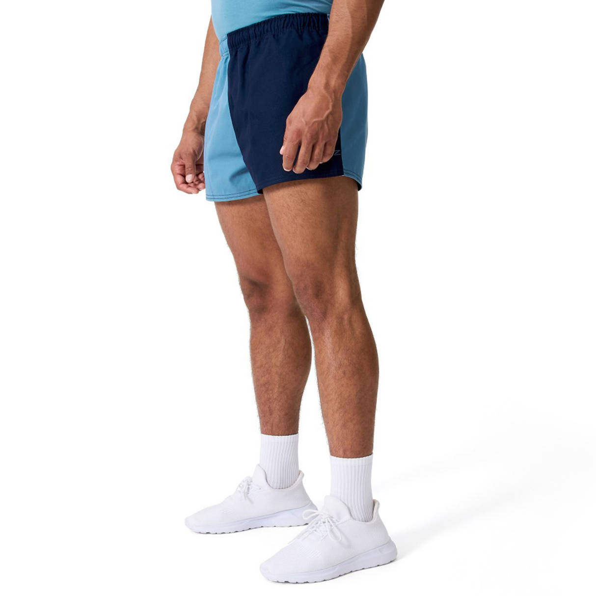 A person in a light blue shirt, Canterbury Fundamental Harlequin Drill 3" Shorts in two-tone blue, white crew socks, and white sneakers stands against a plain white background.