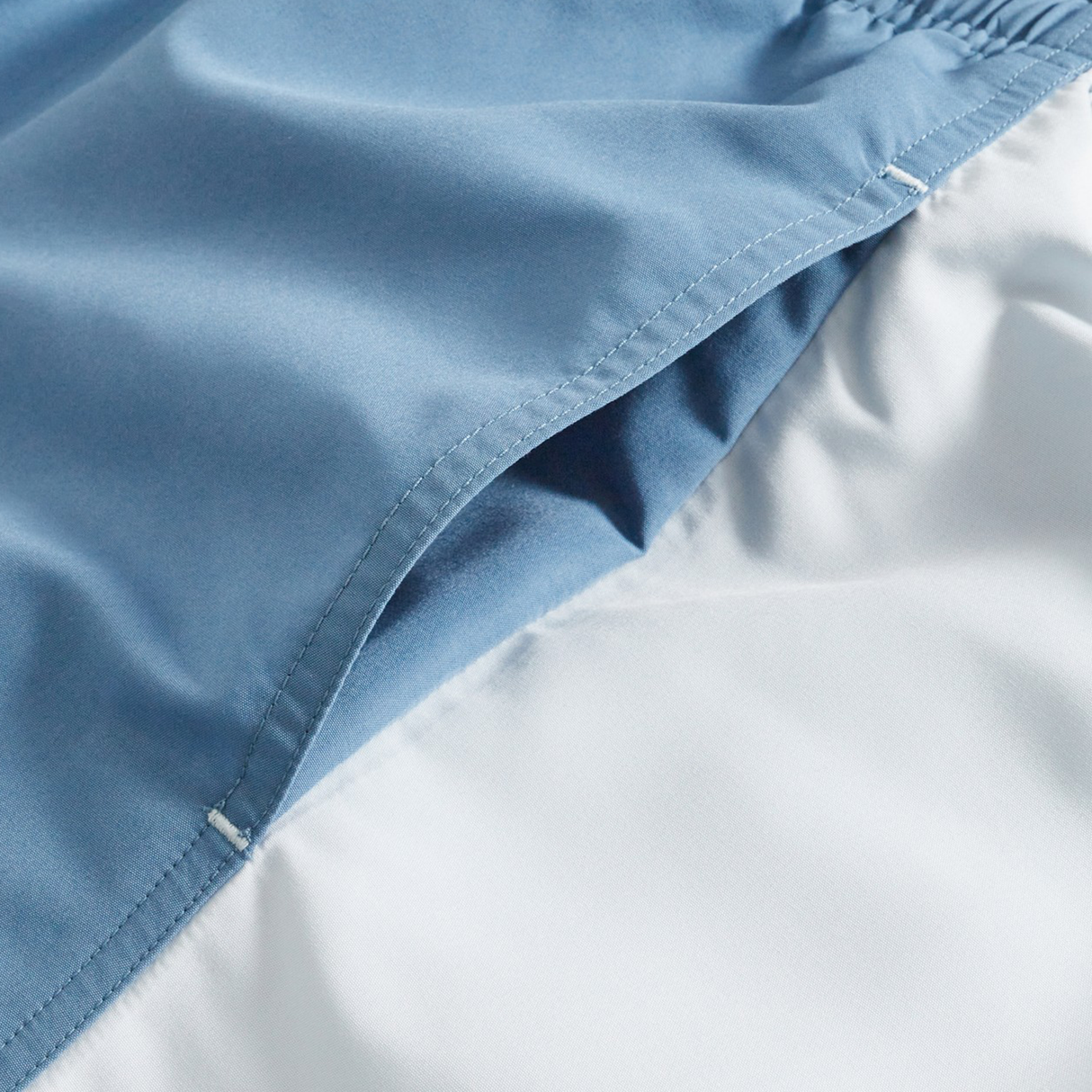 Close-up of Canterbury Fundamental Harletic 3" Shorts highlights the blue outer fabric, white lining, visible stitching, and overlapping seam.