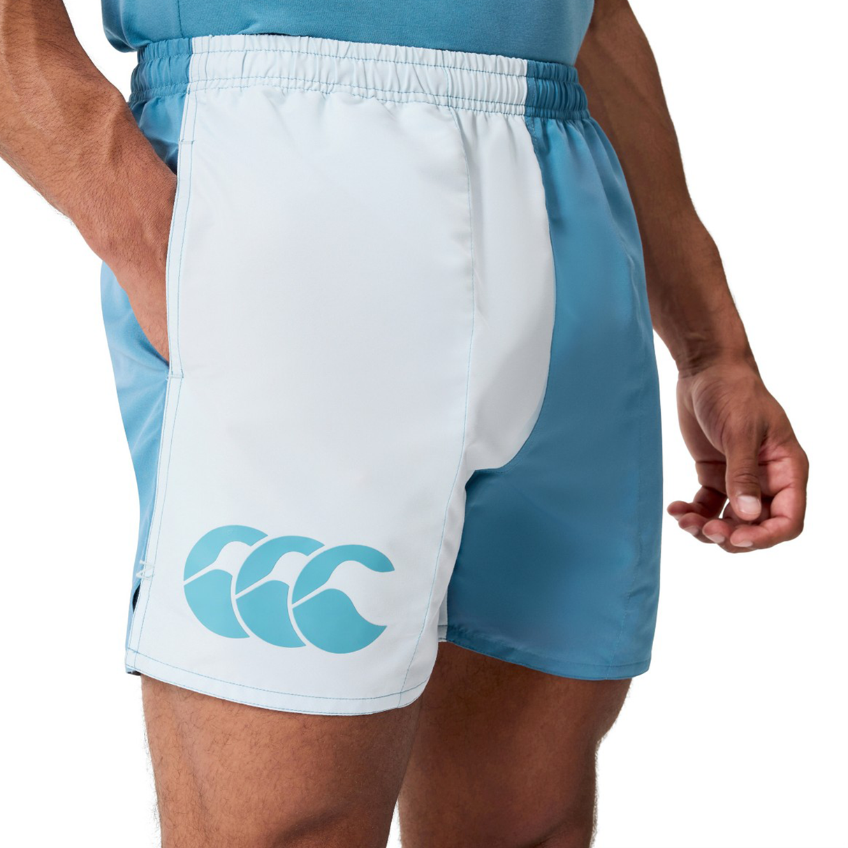 A person wearing Canterbury Fundamental Harletic 3" Shorts in light blue and white, featuring an elastic waistband and the CCC logo on the left leg.