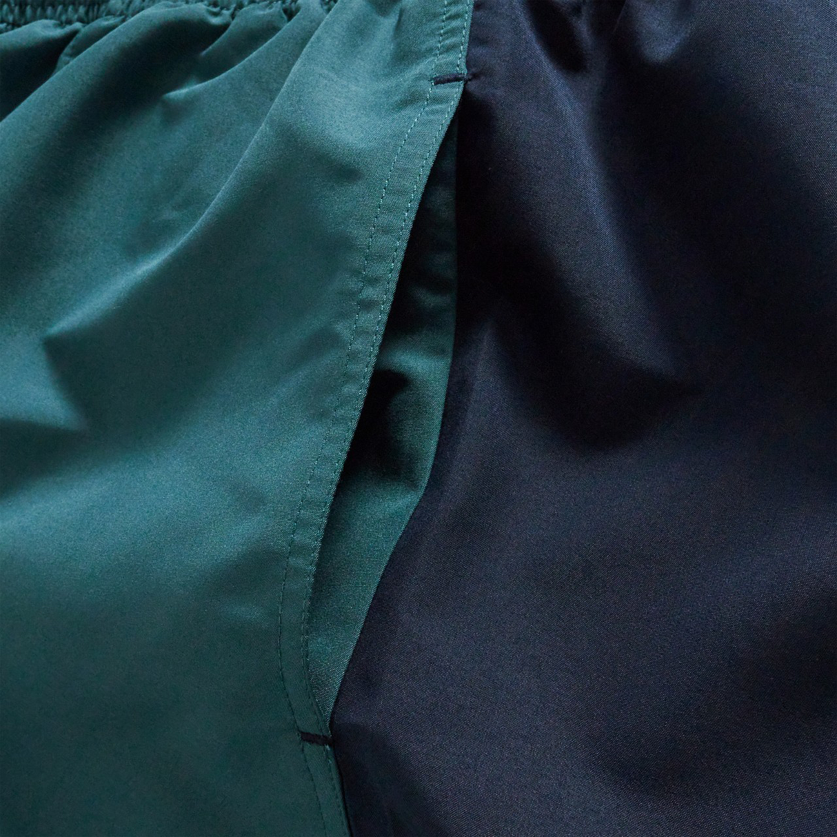 Close-up of the Fundamental Harletic 3" Shorts by Canterbury, featuring dark green and black fabric with a visible seam and gathered elastic waistband, reminiscent of classic Canterbury rugby shorts.