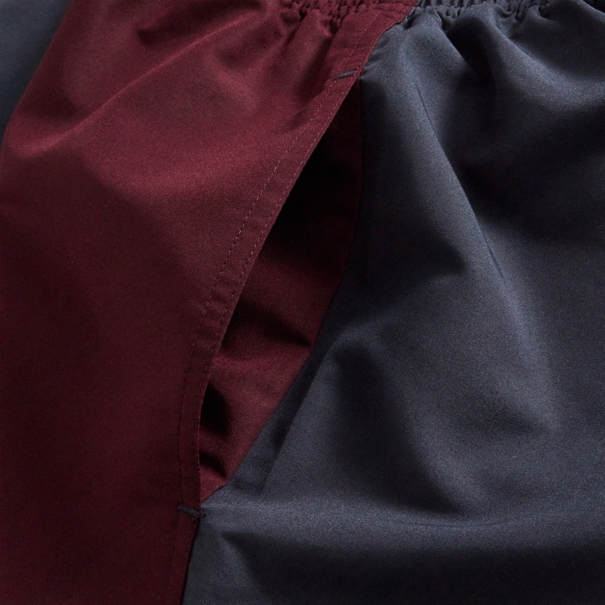 Close-up of Canterbury Fundamental Harletic 3" Shorts highlighting the side pocket and elastic waistband, crafted from maroon and dark gray fabric.