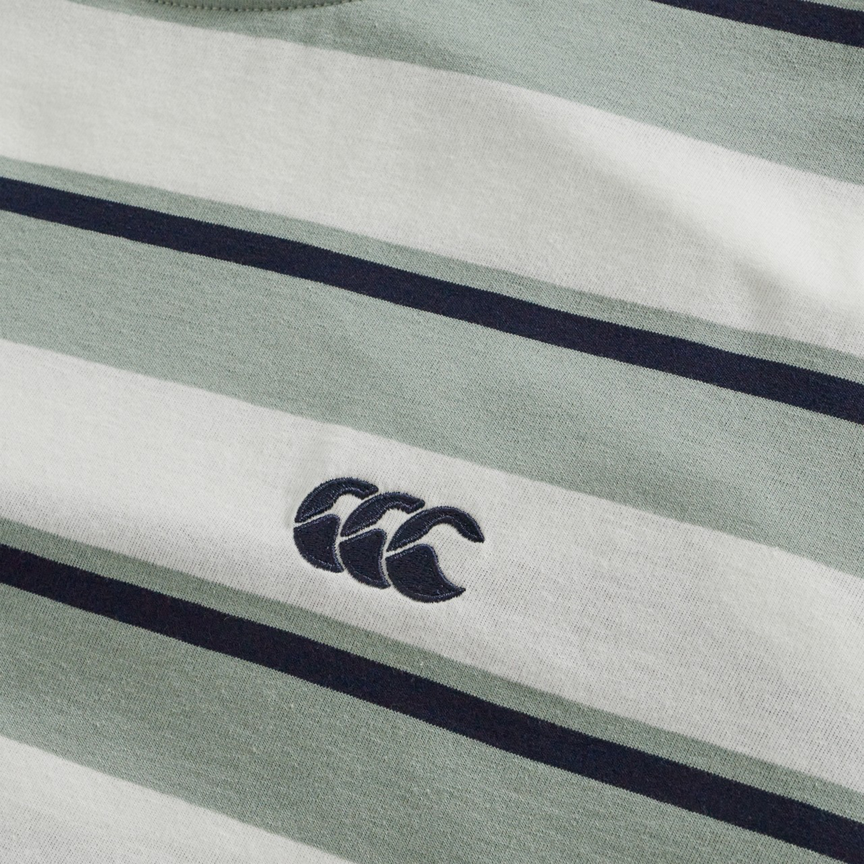 Close-up of the Canterbury Fundamental Yarn Dye Stripe T-Shirt in green, white, and dark blue, with a small embroidered three-curve logo—ideal for a rugby-inspired style.