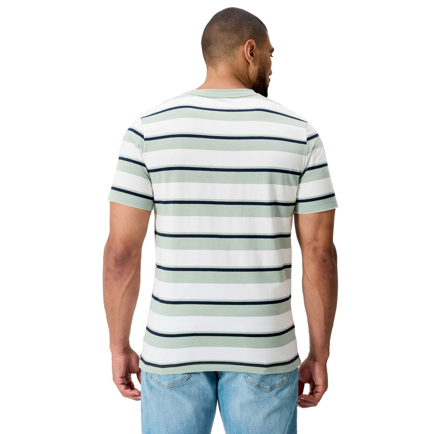 A man faces away, wearing Canterbury's Fundamental Yarn Dye Stripe T-Shirt—a rugby-inspired white short-sleeve tee with black and green stripes—paired with light blue jeans against a plain white background.