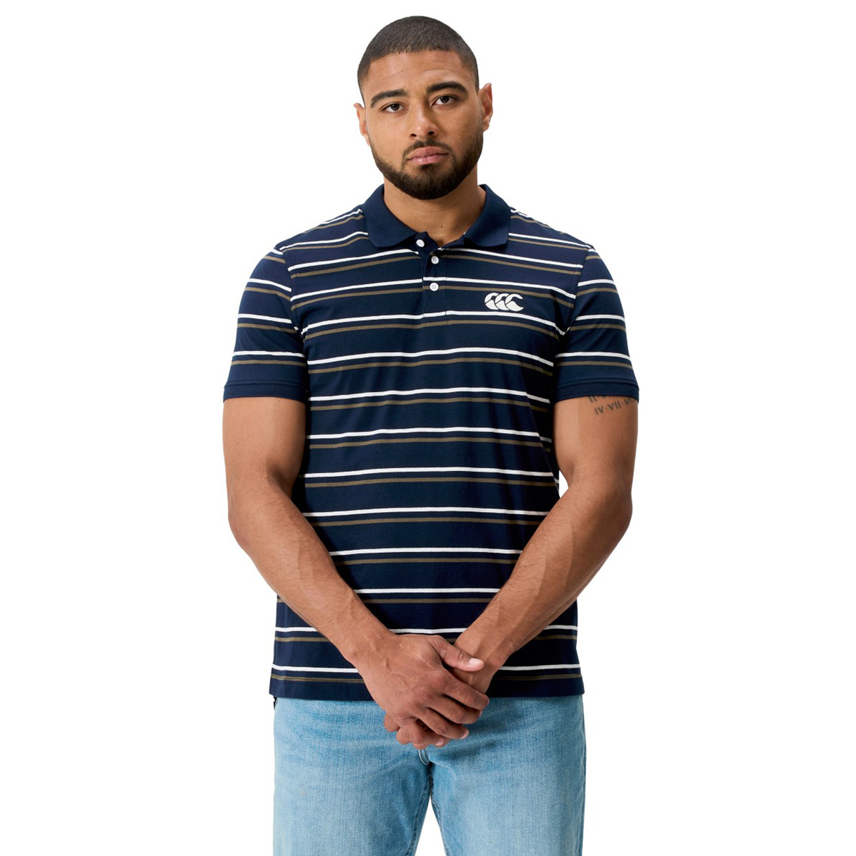 Man standing with hands clasped, wearing the Fundamental Yarn Dye Stripe Polo by Canterbury in navy blue and white, paired with light blue jeans, facing forward against a white background.