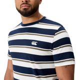 A man stands against a plain background wearing the Canterbury Fundamental Yarn Dye Stripe T-Shirt in navy, white, and olive green, featuring a small white chest logo and showcasing its rugby-inspired style.