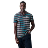 A man stands against a white background wearing the Canterbury Yarn Dye Stripe Polo from Canterbury, inspired by rugby heritage, paired with dark jeans and with one hand in his pocket.